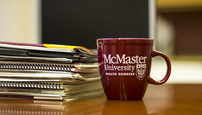 McMaster coffee cup on a desk beside a stack of papers