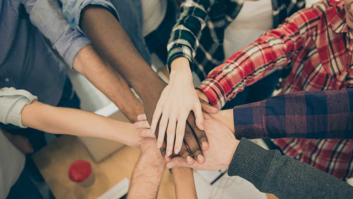 A group of people hold their hands on top of one another., positioned in a circle.